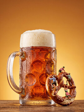 Miniature Oktoberfest people climbing pretzel by cold beer mug