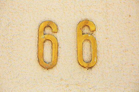 66 house number in metal digits mounted on cracked painted wall, vintage address plaque with peeling paint and weathered rustic texture closeup