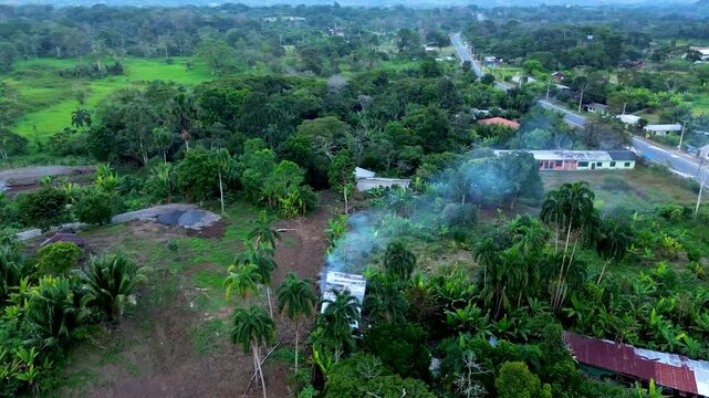 Aerial View of Tropical Ecuador Countryside with Smoke, Palm Trees, Forest Edge, Rural Houses and Green Mountain Valley Landscape