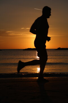 Silhouetted runner in mid stride on the beach against a glowing orange sunrise sky