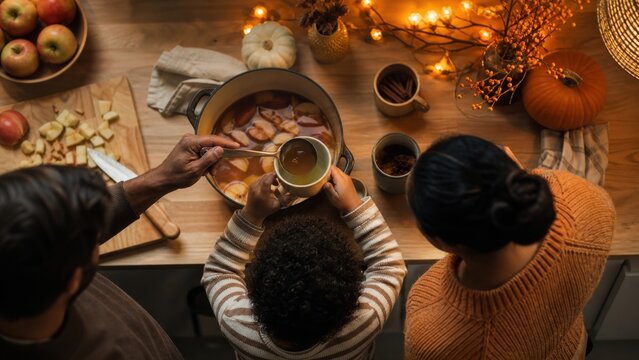 A family preparing warm apple drinks in a kitchen decorated with understated orange accents, candid medium action view, for holiday campaigns