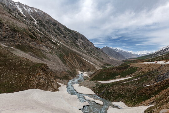 View of Gittidas Valley featuring a winding river flowing through a rugged mountain landscape with patches of snow and rocky slopes in Gittidas, Khyber Pakhtunkhwa, Pakistan.