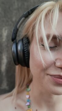 Vertical video of young adult Caucasian woman wearing wireless headphones, smiling with closed eyes while listening to music. Clip is ideal for promoting audio streaming apps or podcast platforms