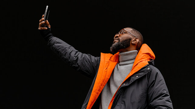 Man takes selfie while standing against a dark background during an outdoor event