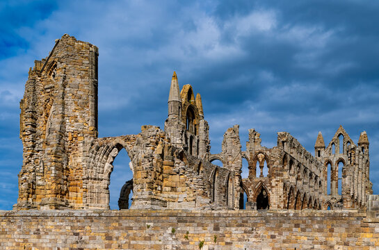 Historic ruins of Whitby Abbey overlooking the coastal town of Whitby in North Yorkshire, England, beneath a dramatic blue-grey summer sky.