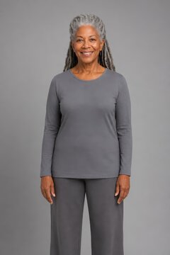 Grey haired woman with long locs smiling against a plain backdrop