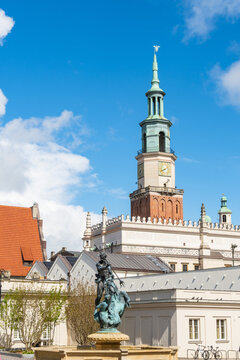 View of the historic Poznan Town Hall with its prominent clock tower, featuring the Proserpina Fountain in the foreground under a bright blue sky in Poznan, Greater Poland Voivod, Poland.