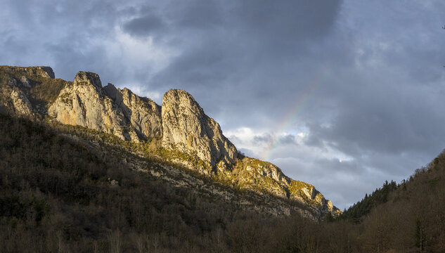 View of the rocky peaks of Isaba illuminated by golden light with a faint rainbow appearing against dramatic storm clouds in Isaba, Navarre, Spain.