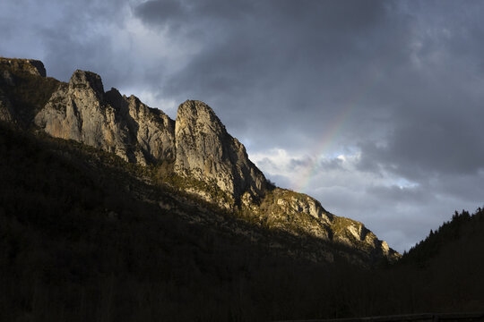 View of the rocky peaks of Isaba with a faint rainbow appearing under dramatic storm clouds in the Pyrenees, Isaba, Navarre, Spain.