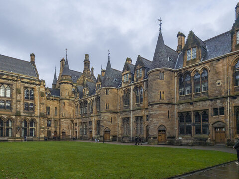 View of the historic Gothic revival architecture of the University of Glasgow with its stone turrets and green courtyard in Glasgow, Scotland, United Kingdom.
