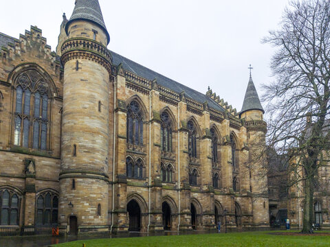 View of the historic University of Glasgow with its intricate Gothic Revival architecture, stone towers, and pointed arches set against an overcast sky in Glasgow, Scotland, United Kingdom.