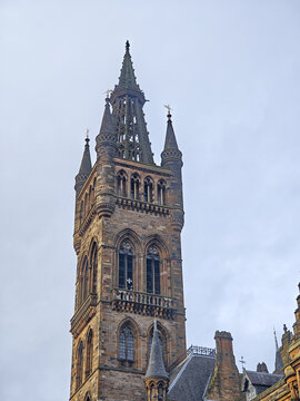 View of the historic Gothic Revival tower of the University of Glasgow with intricate stonework and pointed arches against a cloudy sky in Glasgow, Scotland, United Kingdom.