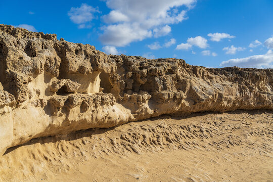 View of the rugged limestone cliffs and caves at Ajuy, featuring weathered rock formations under a bright blue sky with scattered clouds in Ajuy, Fuerteventura, Spain.