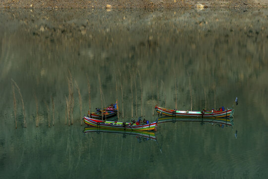 View of colorful wooden boats floating on the turquoise waters of Attabad Lake with submerged tree trunks in the background in Hunza, Pakistan.