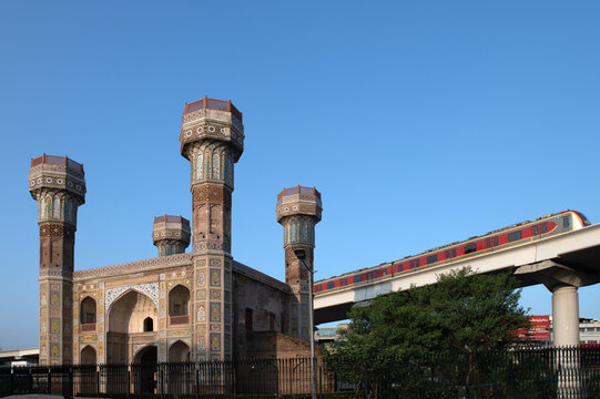 View of the historic Chauburji monument with its intricate tile work and four towers, juxtaposed with a modern metro train on an elevated track in Lahore, Punjab, Pakistan.