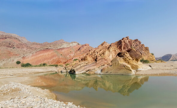 View of the colorful layered rock formations of the Koh-e-Sulaiman mountain range reflecting in a calm pool of water in Gulki, Punjab, Pakistan.