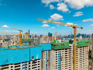 Large construction cranes operate on high rise buildings during the urban development of the city skyline in Wuhan China under a bright blue sky with white clouds © AS_SleepingPanda