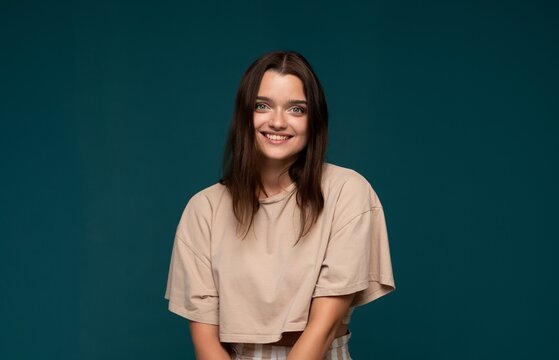 Young smiling woman posing in beige crop top and striped pants, expressing happiness and positive emotion on teal background