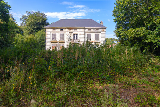 Urbex d'un manoir ou ch&acirc;teau ancien abandonn&eacute; partiellement masqu&eacute;e par de hautes herbes et une v&eacute;g&eacute;tation dense en friche.