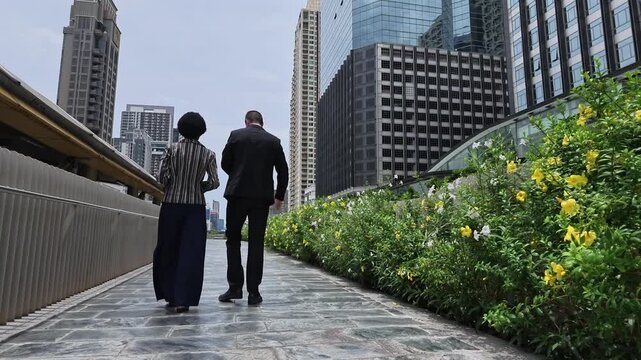 Couple walking hand in hand along a city path with greenery and modern skyscrapers in the background