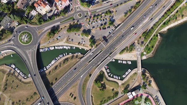 Top down aerial view of a road interchange with a roundabout, moving traffic and a waterway in Koper, Slovenia, revealing modern urban infrastructure from above.