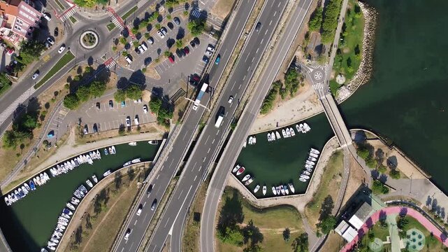 Top down aerial view of a road interchange with a roundabout, moving traffic and a waterway in Koper, Slovenia, revealing modern urban infrastructure from above.