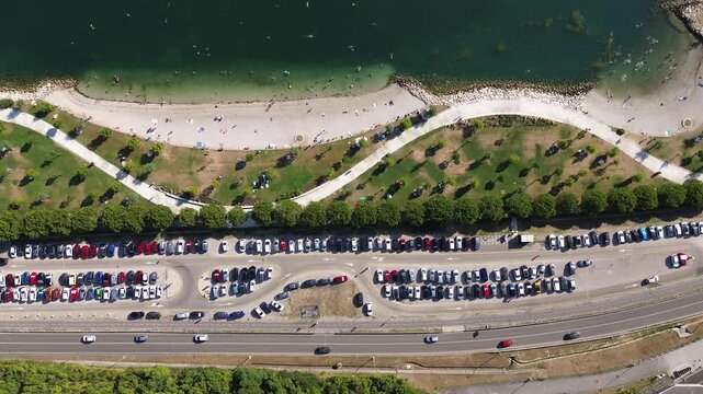 Top down aerial view of the Koper coastline in Slovenia featuring a beach, green hillside, busy coastal road, parked cars and the Adriatic Sea.