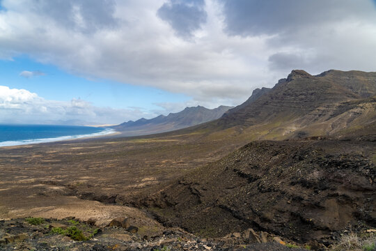 View of the dramatic volcanic mountains and the expansive coastline of Cofete beach under a cloudy sky in Cofete, Canary Islands, Spain.