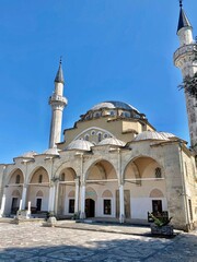 Historic mosque with domes and slender minarets rises beneath clear blue sky. © Allanimaa
