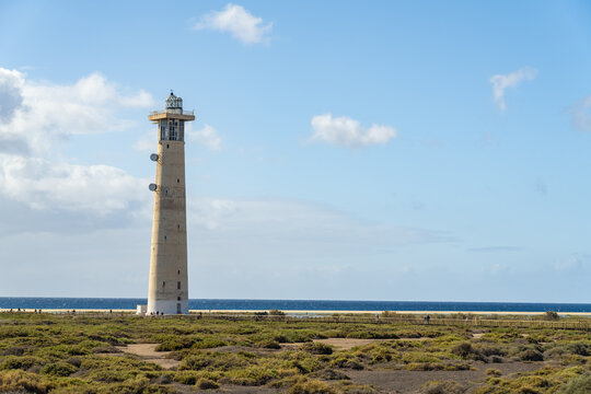 View of the Morro Jable Lighthouse standing tall amidst the coastal landscape with sparse vegetation and the blue sea in the background in Morro Jable, Canary Islands, Spain.