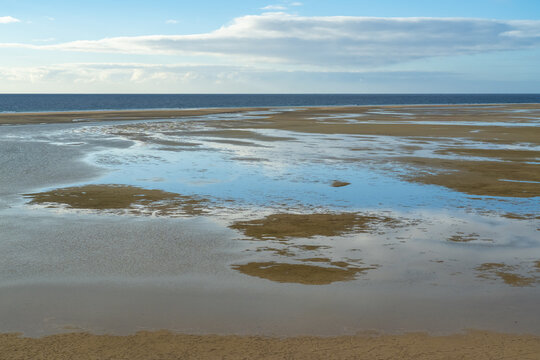 View of Jandia beach at low tide with shallow pools of water reflecting the sky and horizon in Jandia, Canarias, Spain.