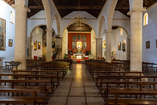 View of the interior of the historic Church of Nuestra Senora de la Candelaria featuring wooden pews, stone columns, and an ornate altar in La Oliva, Canary Islands, Spain.