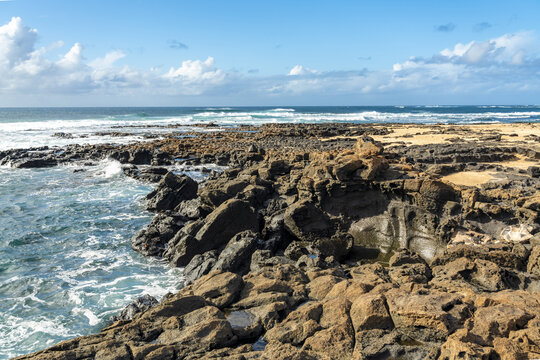 View of the rugged volcanic rock coastline and Atlantic Ocean waves at El Cotillo, Canary Islands, Spain.