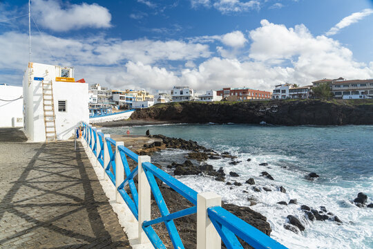 View of the coastal village of El Cotillo with white buildings, blue wooden railings, and rocky shoreline overlooking the turquoise Atlantic Ocean in El Cotillo, Canary Islands, Spain.