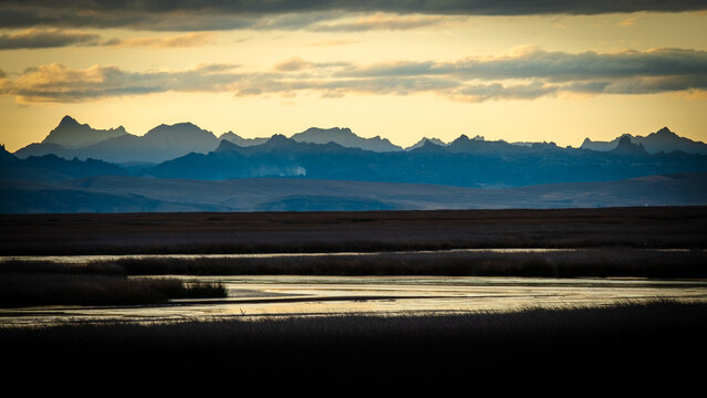 View of the Huascaran mountain range in the Andes at sunset with golden light illuminating the dramatic sky above the wetlands in Yungay Province, Ancash, Peru.