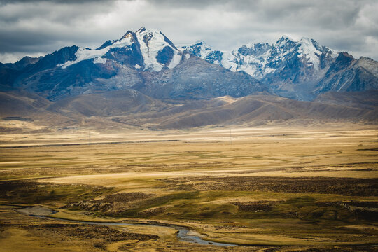 View of the snow-capped Huascaran mountain range rising above the vast arid plains and winding river in Yungay Province, Ancash, Peru.