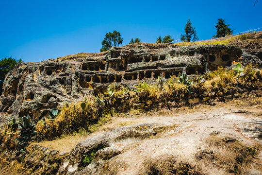 View of Ventanillas de Otuzco, an ancient archaeological site with rock-cut tombs carved into volcanic cliffs, surrounded by cacti and dry Andean landscape in Cajamarca, Cajamarca, Peru.