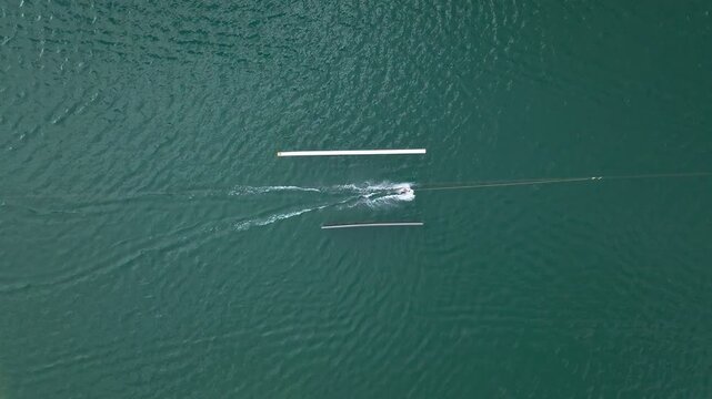 Aerial top-down view of a person wakeboarding between obstacles on a big lake with water-skiing course