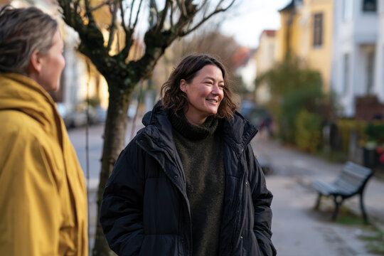 Two friends enjoying a casual conversation while standing on a vibrant street, surrounded by trees and buildings, capturing a moment of connection and joy.