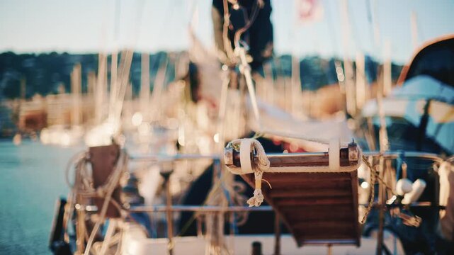 Wooden gangplank resting on sailboat deck at sunset with blurred yacht masts in background marina.