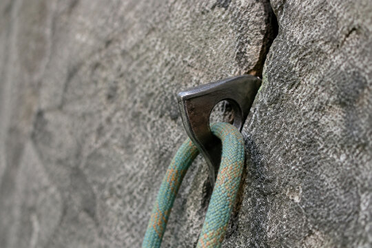 A steel climbing piton in granite with a rope, natural daylight.