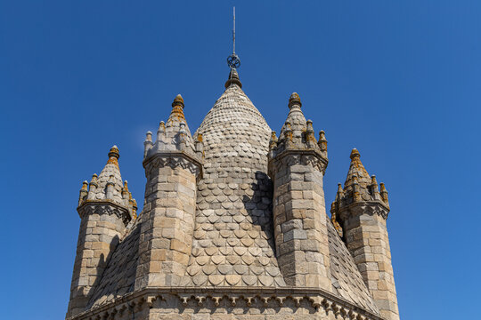 View of the stone spire of the Cathedral of Evora with its distinctive scale-like masonry and pinnacles against a clear blue sky in Evora, Distrito de Evora, Portugal.