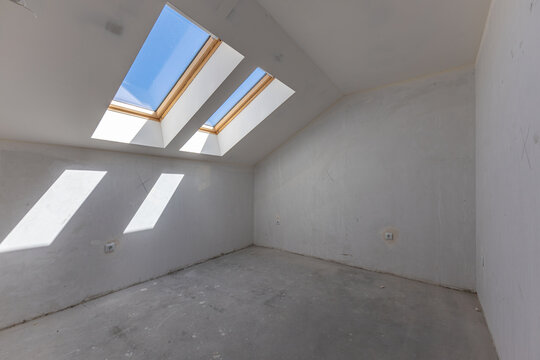 Empty Attic Room Under Renovation with Double Skylight Windows Flooding. Dormer windows. Interior shot of a roof windows.