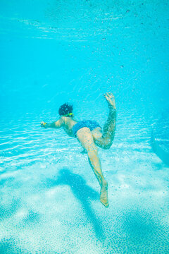 Boy gliding underwater above curved steps in clear resort swimming pool. Concept of youth sports, swimming instruction and family travel.