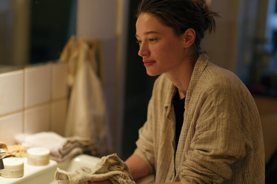 Captured in a serene bathroom setting, a woman reflects during her skincare routine, emphasizing self-care, beauty rituals, and moments of quiet reflection.