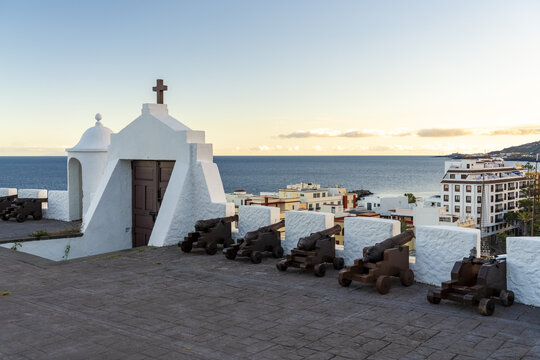 View of historic cannons lined up on the white stone walls of the Castillo de Santa Catalina overlooking the sea and the town of Santa Cruz de La Palma, Canary Islands, Spain.