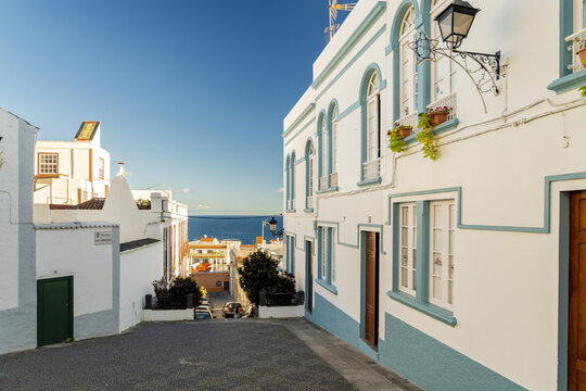 View of traditional white buildings with blue trim lining a cobblestone street leading towards the sea in Santa Cruz de La Palma, Canary Islands, Spain.