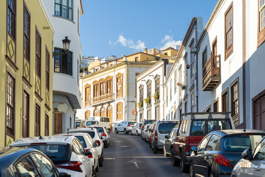 View of the historic street lined with colorful colonial buildings and parked cars under a clear blue sky in Santa Cruz de La Palma, Canary Islands, Spain.