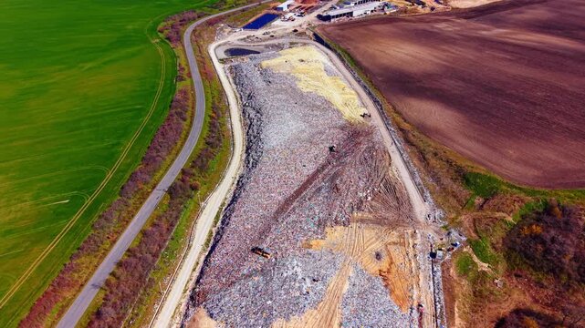 Landfill site next to agricultural field. Drone view of waste disposal area bordered by green and brown farm lands.