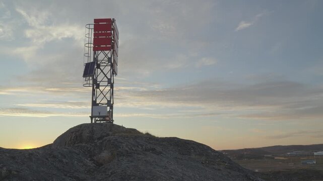 Low-angle shot focusing on a red-and-white navigational warning tower and communications mast standing on an exposed granite outcrop above the city.